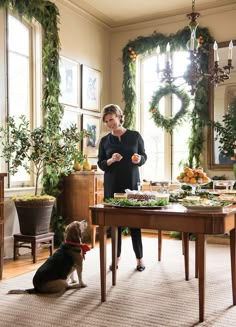 a woman standing in front of a table with food on it and a dog sitting next to her