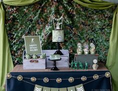 a table topped with cakes and cupcakes under a green curtain