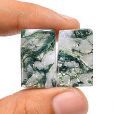 a hand holding two square shaped green and white marbles on it's fingers