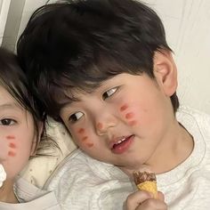 two young children laying down eating food and looking at the camera with freckles on their faces