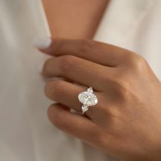 a woman's hand with a diamond ring on her left hand, wearing a white shirt