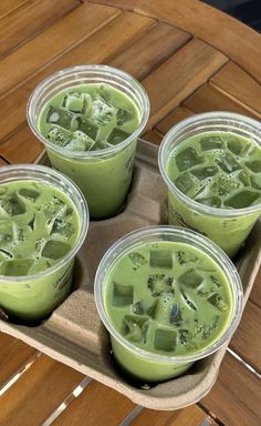 four cups filled with green liquid on top of a wooden table