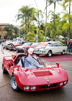 a red sports car parked on the side of a road next to other cars and people