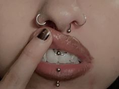 a close up of a person with piercings on their nose and lip, touching the tip of her nose