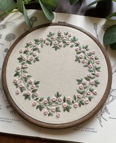 a white embroidered circle with pink flowers and green leaves on top of a piece of paper