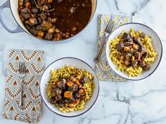 three bowls of pasta with meat and vegetables on a marble countertop next to a pot of stew