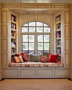 a window seat with pillows on it in front of a bookshelf