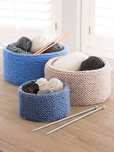 three knitted baskets on a table with knitting needles