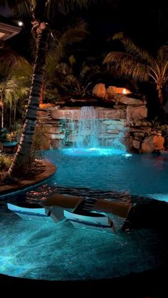 an outdoor pool at night with waterfall and lounge chairs in the foreground, surrounded by palm trees