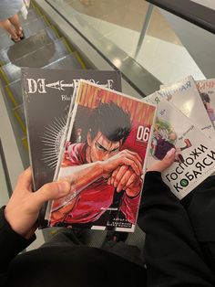 a person holding up some anime books in their hands while riding an escalator