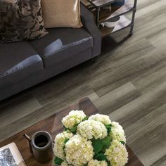 a coffee table with white flowers on it in front of a gray couch and chair