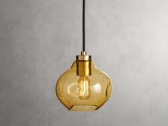 a yellow glass light bulb hanging from a black cord on a gray wall with concrete background