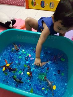 a young boy playing in a blue tub filled with water and plastic toys on the floor