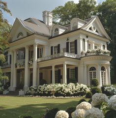 a large white house with lots of windows and flowers in the front yard, on a sunny day