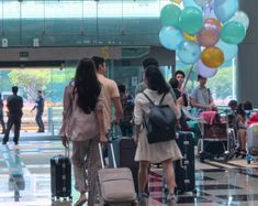 several people are walking through an airport with luggage and balloons in the air above them