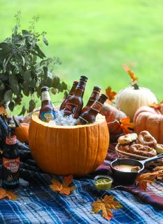 beer bottles in a pumpkin bowl on a table with fall leaves and other food items