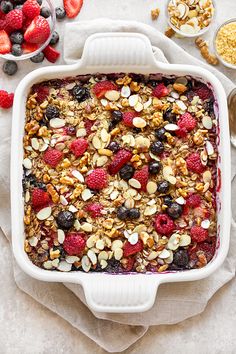 a white casserole dish filled with granola, berries, nuts and blueberries