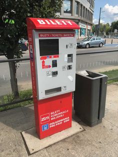 a red and white machine sitting on the side of a road next to a trash can