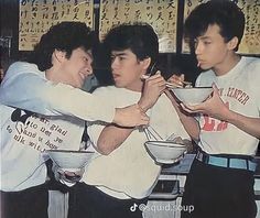 three young men standing together eating food from bowls and chopsticks in front of them