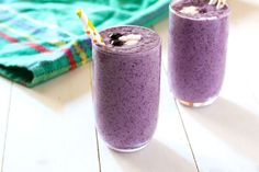 two glasses filled with blueberry smoothie on top of a table