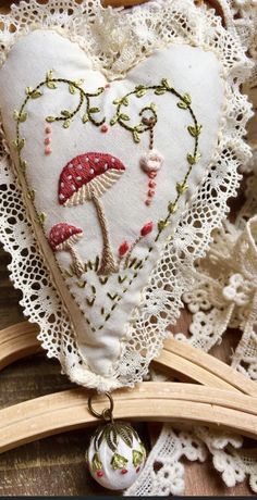 an embroidered heart with mushrooms and leaves on it, sitting next to lace doily