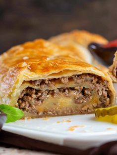 a piece of meat filled pastry sitting on top of a white plate next to some olives