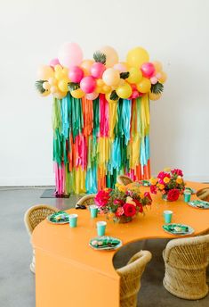 an orange table topped with lots of colorful balloons and streamers on top of it