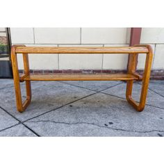 a wooden bench sitting on top of a cement floor next to a building with a brick wall