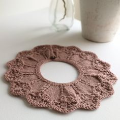 a crocheted doily sits on a table next to a cup and vase