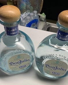 two bottles of tequila are sitting on a counter top, one is empty and the other has a wooden lid