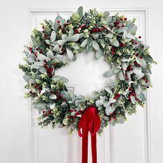 a wreath with red ribbon hanging on the front door decorated with greenery and berries