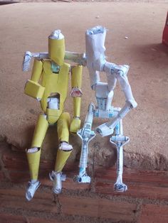 two toy robots sitting next to each other on top of a brick wall and floor