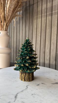 a small green christmas tree sitting on top of a white table next to a vase