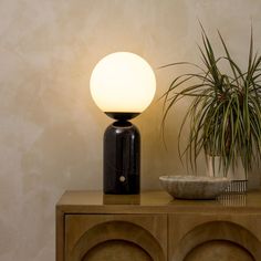 a lamp sitting on top of a wooden cabinet next to a potted plant