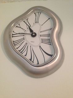 a silver clock with black and white designs on it's face is hanging from the wall