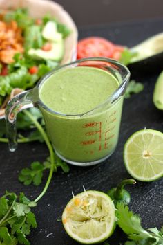 a green smoothie in a blender surrounded by limes, tomatoes and cilantro