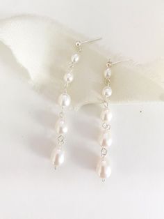 the earrings are made with white pearls and silver wire, on top of a white cloth