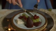 a person holding a knife and fork over a plate with fruit on top of it