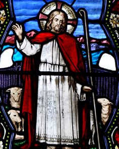 a stained glass window with a man holding a cross and sheep in front of him