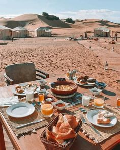 a table set with food and drinks on the beach in front of some sand dunes