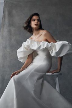 a woman in a white dress sitting on a chair with her hands on her hips