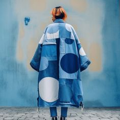 a woman standing in front of a blue wall wearing a jacket with white polka dots on it