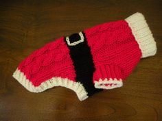 a red and white knitted dog sweater on a wooden floor with a black belt