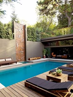 an outdoor swimming pool with lounge chairs and tables next to it, surrounded by greenery