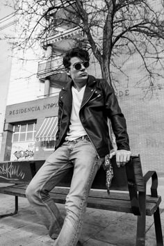 a young man sitting on top of a wooden bench next to a tree and building