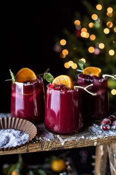 three glasses filled with red liquid and garnished with orange slices on a table next to a christmas tree