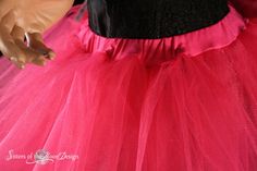 a doll wearing a pink tutu skirt and black top with white nails on her finger