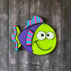 a green fish with purple and pink stripes on it's head is mounted to the side of a wooden wall