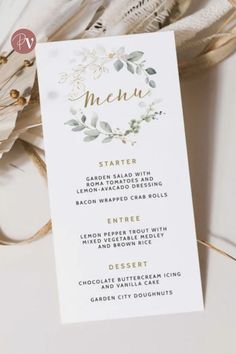 a white menu card with gold foil lettering and greenery on the front, sitting next to some feathers