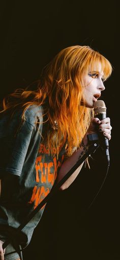 a woman with long red hair holding a microphone in her right hand and singing into the microphone